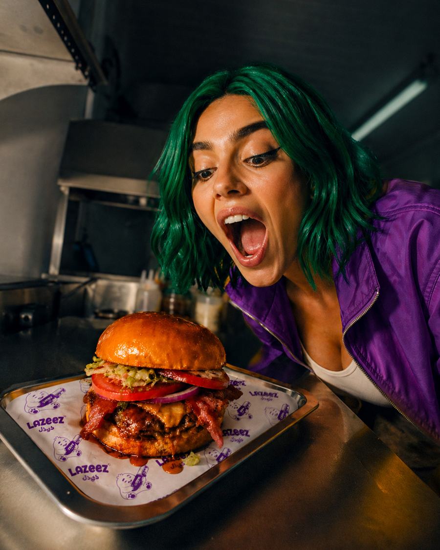 Chef seasoning a Lazeez sandwich in moody lighting